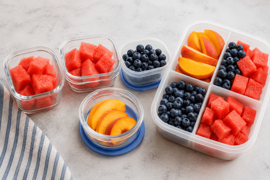 Meal prep containers filled with sliced peaches, blueberries, and watermelon for easy back-to-school breakfasts, lunches, and snacks
