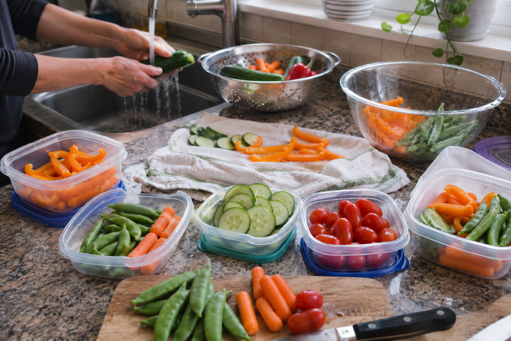 Fresh carrots, cucumbers, bell peppers, snap peas, and tomatoes washed and portioned into containers for school lunches