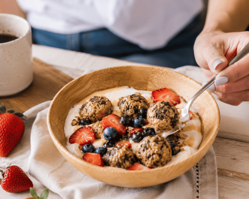 Fit Five Meals Protein Bites served in a Greek yogurt parfait with fresh strawberries, blueberries, granola, and honey in a wooden bowl